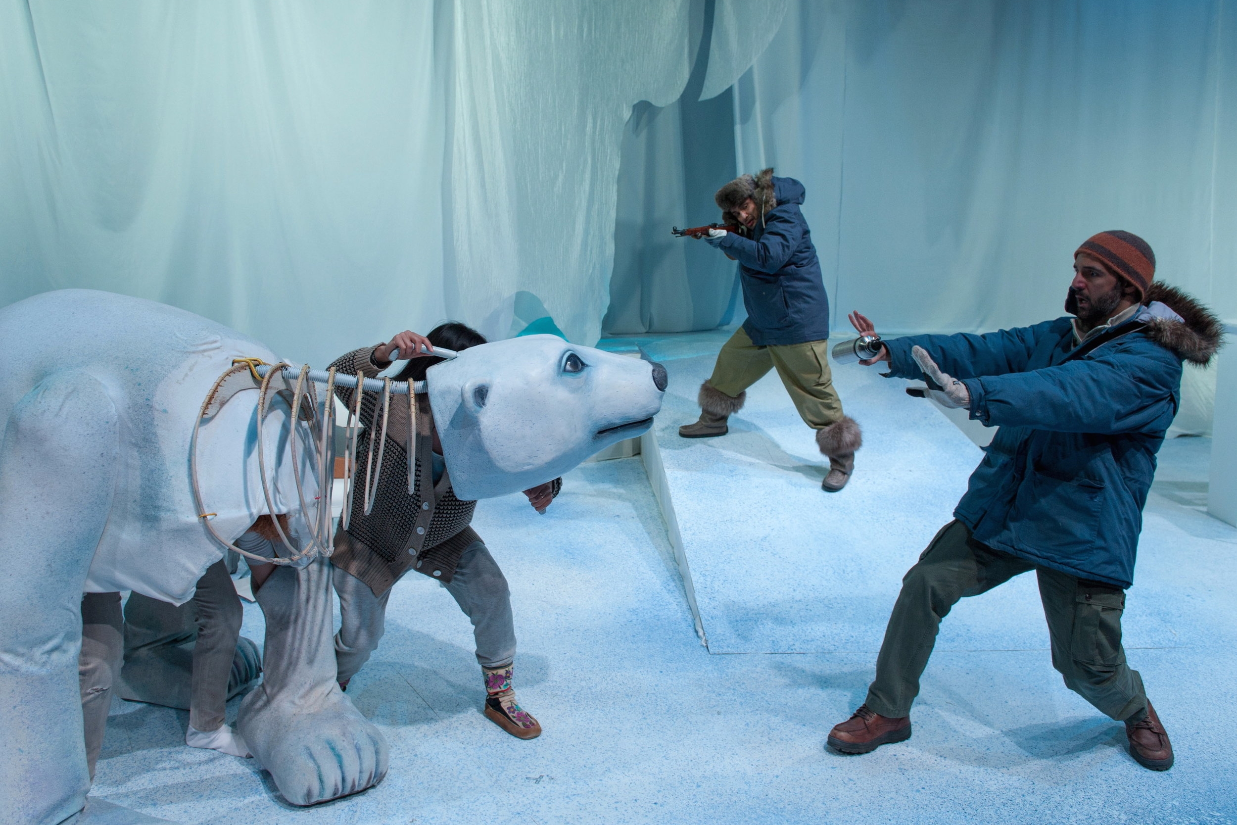 A person next to a puppet polar bear while a person with a gun stands in the background