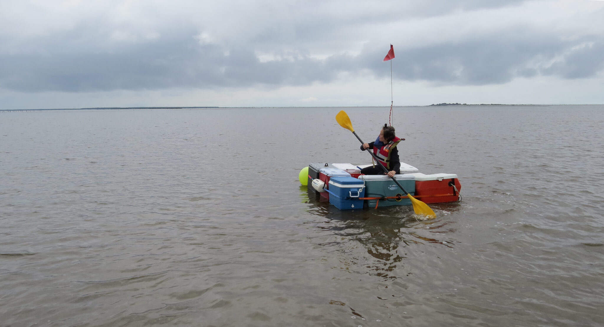 a life raft constructed from coolers floating in the ocean with a person riding it